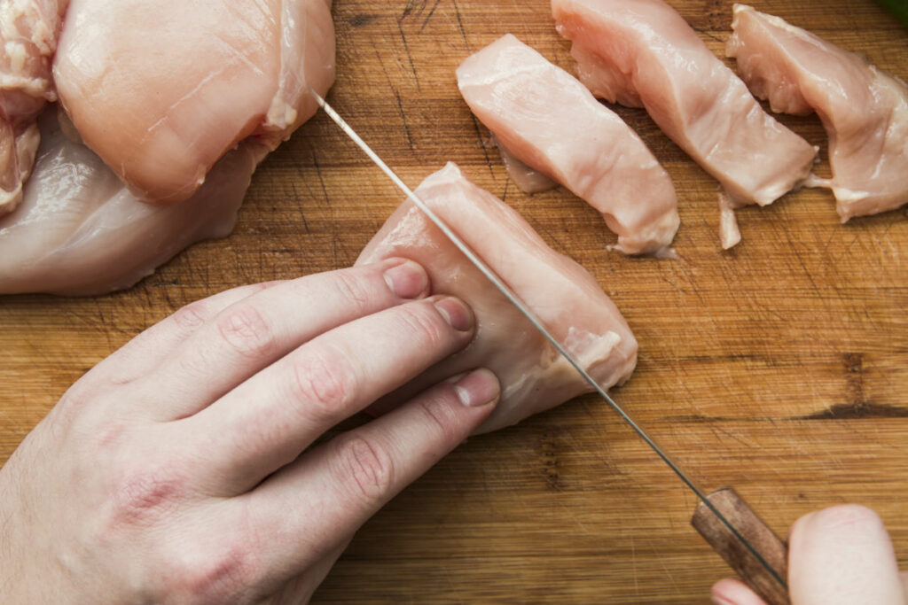 Cutting raw chicken on chopping board